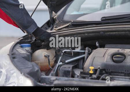 Auto Mechanic dévisse le bouchon du vase d'expansion pour verser l'antigel dans l'atelier d'entretien automobile Banque D'Images