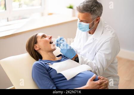 Dentiste masculin traitant les dents de la jeune femme enceinte Banque D'Images