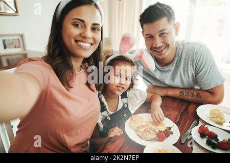 Immortalisez les petits déjeuners en famille. Photo d'un jeune couple prenant un selfie tout en prenant le petit déjeuner avec leur fille à la maison. Banque D'Images