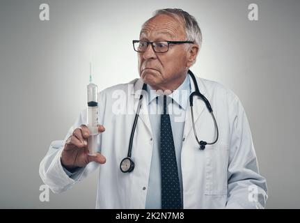 Ce nouveau traitement est tout à fait merveilleux. Cliché d'un médecin âgé tenant une seringue pour injection dans un studio sur fond gris. Banque D'Images