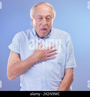 L'essoufflement pourrait raccourcir votre vie, faites-le vérifier. Photo en studio d'un homme âgé souffrant d'une gêne thoracique sur fond bleu. Banque D'Images