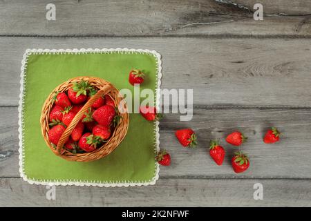 Photo de table, panier de fraises , certains d'entre eux renversé sur une nappe verte et grise bureau en bois. Banque D'Images