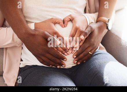 Enveloppé d'amour. Photo courte d'un couple affectueux et méconnaissable de parents assis sur le canapé à la maison. Banque D'Images