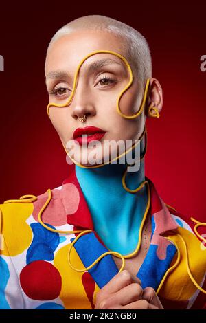 Tout ce que je veux faire, c'est d'étendre un peu de couleur. Photo studio d'une jeune femme élégante posant sur un fond rouge. Banque D'Images