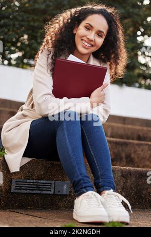 Prêt pour ma prochaine classe. Portrait d'une jeune étudiante d'université attrayante assise à l'extérieur du campus pendant sa pause. Banque D'Images