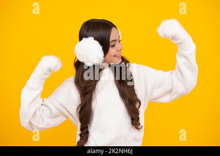 Magnifique portrait d'hiver pour enfants. Adolescente posant avec un chandail d'hiver et un cache-oreilles chaud d'hiver sur fond jaune. Heureux visage, positif Banque D'Images