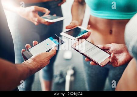 Synchroniser leurs programmes d'entraînement. Gros plan d'un groupe de personnes utilisant leur téléphone portable ensemble à la salle de gym. Banque D'Images