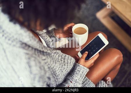 Que font mes amis aujourd'hui. Prise de vue d'une jeune femme non identifiable utilisant son téléphone portable tout en appréciant une tasse de café à la maison. Banque D'Images