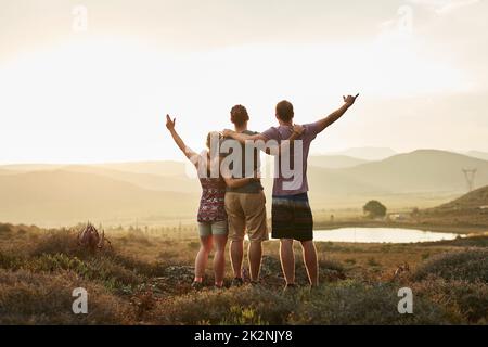 Chaque vue est meilleure lorsqu'elle est partagée avec des amis. Vue arrière de trois randonneurs heureux prenant la vue sur un sentier de montagne. Banque D'Images