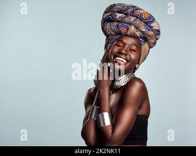 Tout ce qui vous fait briller. Photo studio d'une belle jeune femme portant un casque africain traditionnel sur fond gris. Banque D'Images