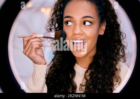 Dites-moi ce que vous pensez de ce regard dans les commentaires. Photo d'une jeune femme qui fait son maquillage tout en enregistrant une vidéo pour son blog. Banque D'Images