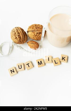 Le lait vegan des noix dans une tasse en verre avec divers noix sur une table blanche. Lettrage de lait de noix. Banque D'Images