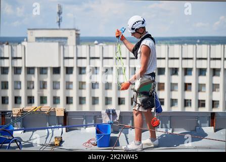Les travailleurs d'alpinisme industriel lavent les fenêtres en verre d'un bâtiment de grande hauteur, travaillant avec des cordes d'escalade sur le toit du gratte-ciel. Banque D'Images