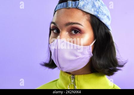 Il est protégé, il reste au frais. Photo studio d'une belle jeune femme portant un masque sur fond violet. Banque D'Images