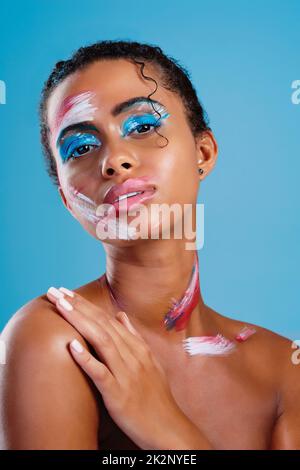 Laissez-moi être votre toile colorée. Studio portrait d'une belle jeune femme couverte de peinture de visage posant sur un fond bleu. Banque D'Images