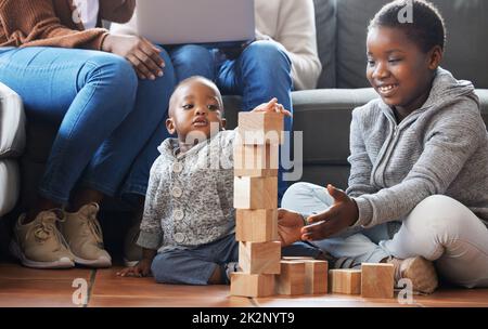 Un petit architecte dans la fabrication. Photo d'une sœur aidant son frère à construire des blocs dans le salon à la maison. Banque D'Images