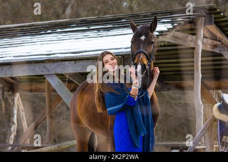 Une fille vêtir d'une robe bleue embrasse un cheval sur fond d'une verrière enneigée dans la forêt Banque D'Images