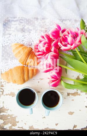 une bonne tasse de café, des croissants et des tulipes roses sur une vieille table blanche, en gros plan Banque D'Images