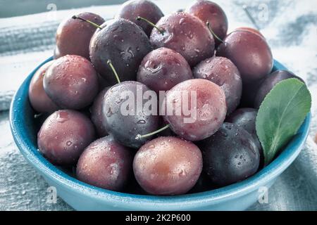 Prunes rouges mûres dans une plaque en céramique bleue Banque D'Images