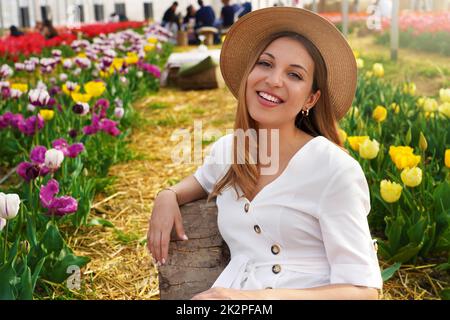 Portrait d'une fille souriante assise détendue entre les champs de tulipes au printemps. Regarder l'appareil photo. Banque D'Images