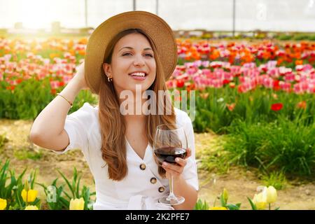 Portrait d'une jolie femme qui boit un verre de vin rouge sur fond fleuri regardant à côté avec le visage souriant Banque D'Images