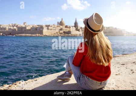 Concept de voyage avec des personnes indépendantes profitant de l'activité de loisirs en plein air et de la vie de Wanderlust style de vie. Une jeune femme s'assoit au bord de la mer et regarde le paysage étonnant de la Valette, à Malte. Banque D'Images