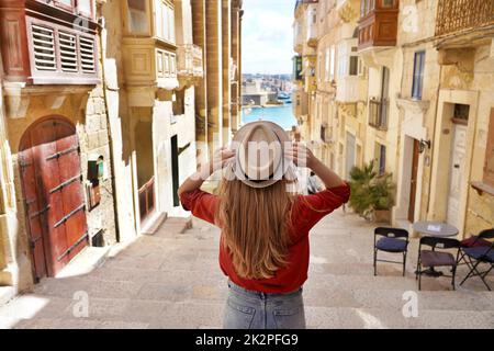 Tourisme à Malte. Vue arrière de la jeune fille touristique tenant le chapeau descend des escaliers dans la vieille ville de la Valette, patrimoine mondial de l'UNESCO, Malte. Banque D'Images