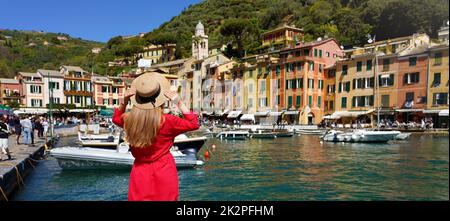 Vacances à Portofino, Italie. Vue arrière de la belle fille en robe rouge profitant de la vue sur le village pittoresque de Portofino avec des navires amarrés et des personnes marchant sur la place Piazzetta, bannière panoramique. Banque D'Images