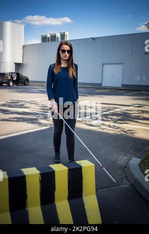 Une jeune femme malvoyante marchant dans les rues de la ville, utilisant sa canne blanche pour mieux naviguer dans l'espace urbain et pour se rendre à destination en toute sécurité Banque D'Images