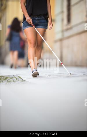 Femme aveugle marchant dans les rues de la ville, utilisant sa canne blanche pour mieux naviguer dans l'espace urbain et pour se rendre à sa destination en toute sécurité Banque D'Images