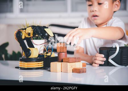 Joyeux petit garçon asiatique utilisant la télécommande jouant le bras de machine robotique pour ramasser le bloc de bois Banque D'Images