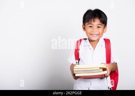 Asiatique adorable tout-petit souriant heureux portant étudiant thaïlandais uniforme pantalon rouge stand livres pour l'étude prêt pour l'école Banque D'Images