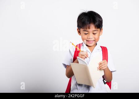 Asiatique tout-petit sourire Happy Wear étudiant thaïlandais uniforme pantalon rouge tenant un crayon pour les écrivains cahier Banque D'Images