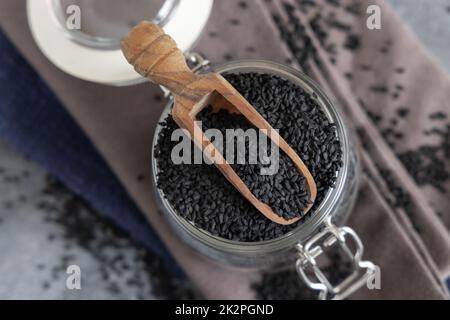 Épices indiennes graines de cumin noir (nigella sativa ou kalonji) dans un pot en verre avec vue sur le dessus de la pelle en bois Banque D'Images