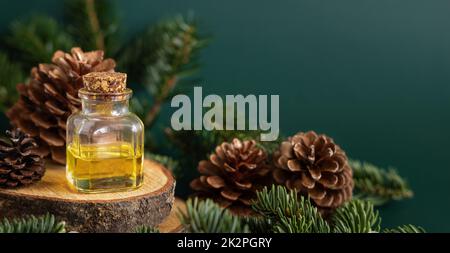 Bouteille en verre avec huile essentielle de conifères près des branches de sapin et des cônes de pin sur le green gros plan Banque D'Images