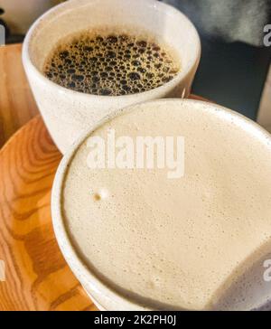 Cappuccino avec mousse de lait parfumée et Americano noir sur un plateau en bois Vue de dessus. Café pour deux. Délicieux café fraîchement préparé pour le petit déjeuner au café Banque D'Images