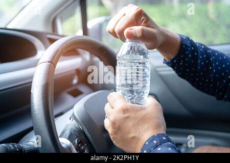 Femme asiatique chauffeur tenant une bouteille pour boire de l'eau tout en conduisant une voiture.Une bouteille d'eau chaude en plastique peut provoquer un incendie. Banque D'Images