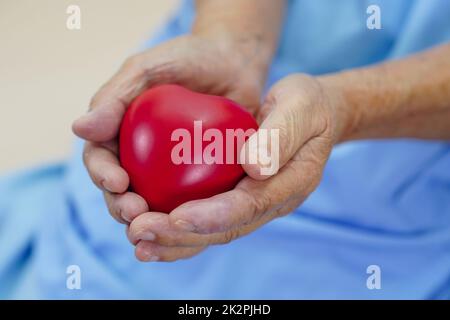 Femme asiatique aînée, patiente portant un cœur rouge à l'hôpital. Banque D'Images