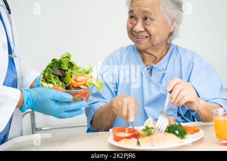 Asiatique senior ou âgée vieille femme patient de manger petit déjeuner légumes nourriture saine avec espoir et heureux tout en étant assis et affamés sur le lit à l'hôpital. Banque D'Images