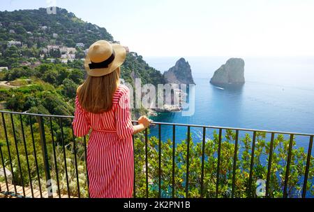 Vacances en Italie. Vue arrière de la belle fille dans la magnifique île de Capri avec la pile de mer Faraglioni et l'eau cristalline bleue sur le fond, Capri, Italie. Banque D'Images