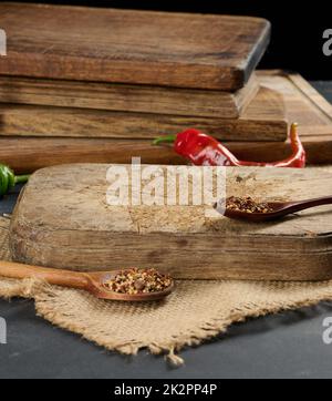 cuisine vide, planche à découper en bois brun sur table noire, à côté de cuillères aux épices et au piment frais, fond noir Banque D'Images