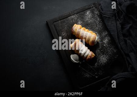 tubes cuits remplis de crème blanche aux œufs fouettés sur un plan de cuisine en bois noir, vue du dessus Banque D'Images