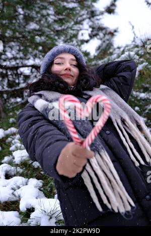 Femme en hiver tenant deux cannes de bonbons formant un coeur bonne année Noël temps Banque D'Images