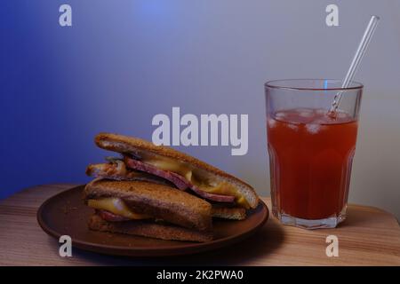 Sandwich avec saucisse et fromage avec soda rouge avec glace dans le verre avec paille du verre Banque D'Images