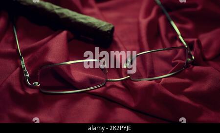 Cigare et lunettes sur satin rouge faible profondeur de champ Banque D'Images