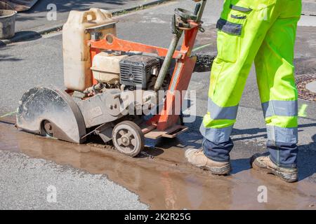 Le travailleur routier coupe le béton avec une machine à découper le béton Banque D'Images