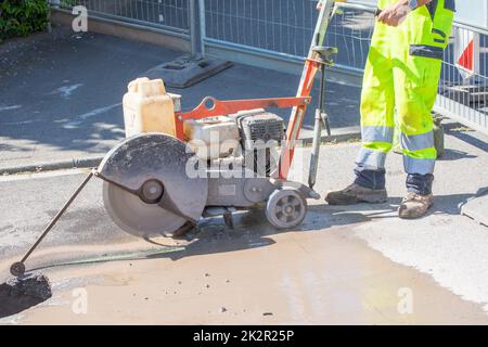 Le travailleur routier coupe le béton avec une machine à découper le béton Banque D'Images