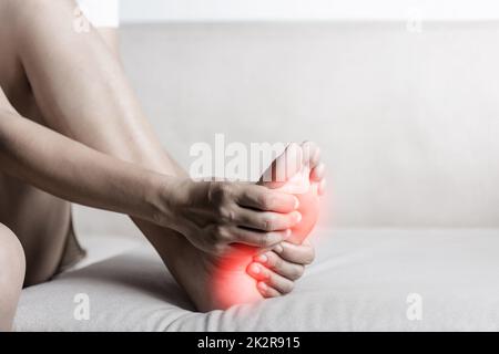 Femme asiatique assise sur un canapé sentant la douleur dans son pied à la maison Banque D'Images