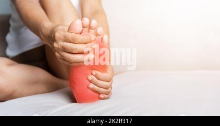 Femme asiatique assise sur un canapé sentant la douleur dans son pied à la maison Banque D'Images