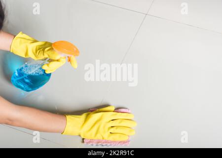 Femme asiatique portant du caoutchouc jaune glover avec chiffon en tissu et détergent spray nettoyant plancher à la maison dans la salle de séjour Banque D'Images